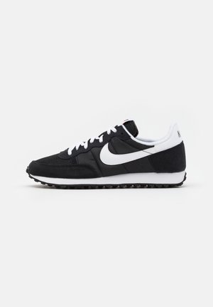 Chaussure de course Nike noire et blanche avec lacets blancs, logo Swoosh blanc et semelle en caoutchouc texturée sur fond blanc uni.