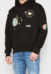 Schwarzer Hoodie mit grafischen Designs eines Globus, Sternen und dem Text "PEGADOR." Mit einer Kängurutasche sowie gerippten Bündchen und Saum.