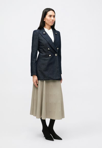 Ναυτικό τζιν διπλό σακάκι με χρυσά κουμπ ιά, σε συνδυασμό με πλισέ μπεζ φούστα, μαύρες καλσόν και μυτερές μαύρες γόβες.