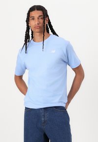 T-shirt en coton bleu clair à manches courtes et col rond. Présente un logo New Balance blanc subtil sur la poitrine gauche.