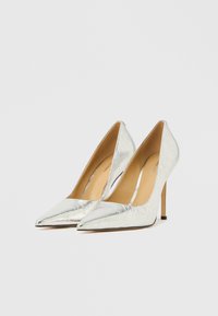 Sølv højhælede pumps med spids tå, lavet af blankt metallisk materiale, med en strømlinet silhuet og en slank stiletthæl.