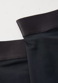 Schwarze Leggings aus Stoff mit glatter Textur, ausgestattet mit einem breiten, dunklen Bund und flachen Nähten, in gefalteter Position angeordnet.