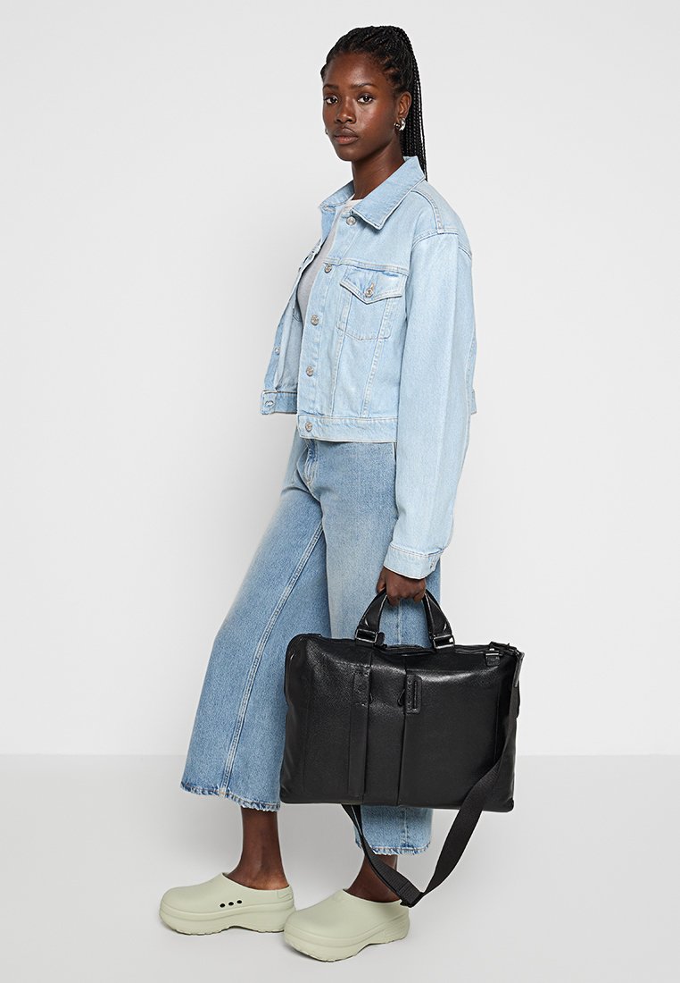 Czarna skórzana torba z podwójnymi uchwytami i regulowanym paskiem, o gładkiej fakturze, prostokątnym kształcie i minimalistycznym wzornictwie.