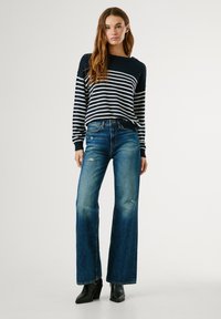 Marineblauw en witte gestreepte gebreide trui, ontspannen pasvorm, gecombineerd met hoogwaisted versleten blauwe flared jeans en zwarte hoge enkellaarsjes.