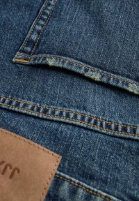 Gros plan sur un tissu en denim bleu avec des coutures orange et une étiquette en cuir marron partiellement visible sur un jean.