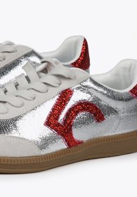 Zapatillas con parte superior metálica plateada, acentos brillantes rojos, puntera de ante gris y forro interior blanco, con una suela de goma texturizada.