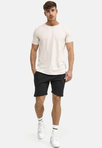 Lichtbeige t-shirt met korte mouwen, zachte textuur, gecombineerd met zwarte shorts, beide casual stijlen. Draag het met witte sneakers en gestreepte sokken.