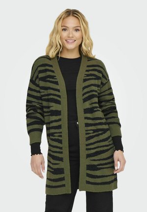 Cardigan vert avec un motif à rayures noires, design à l'avant ouvert, poignets côtelés et un tissu doux et texturé. Porté sur un haut noir.