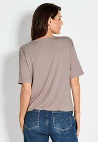 Kurzärmliges, taupefarbenes Oberteil mit lockerer Passform, runden Ausschnitt und glatter Textur, kombiniert mit blauen Denim-Jeans mit genähten Gesäßtaschen.