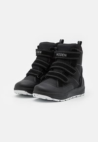 Schwarze Knöchelstiefel mit drei verstellbaren Klettverschlüssen, strukturiertem Synthetik-Obermaterial und einer weißen, robusten Gummisohle für besseren Halt.