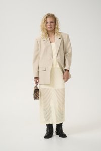 Beige oversized blazer, layered over a pale yellow dress with vertical pleats. Black ankle boots and a small leopard-print handbag.