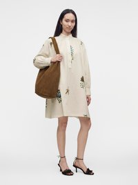 Woman wearing a cream floral dress with long sleeves, black heeled sandals, and carrying a large brown suede shoulder bag.