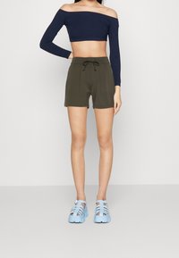 Shorts verde oliva con vita regolabile, abbinati a un top corto blu navy senza spalle. Ai piedi, scarpe azzurro chiaro con cinturino completano l'outfit.