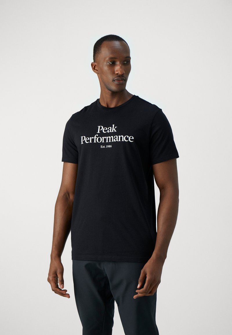 Camiseta de algodón negra de manga corta con el logo "Peak Performance" y "Est. 1986" en texto blanco en la parte delantera.