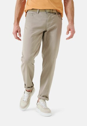 Beige chino pants with a smooth texture, rolled cuffs, and a slim fit, paired with light-colored sneakers and an orange shirt.