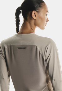 Langarm-Sportoberteil in hellem Beige mit strukturiertem Stoff. Verfügt über ein Rückenteil-Detail und stilvolle Nähte. Geeignet für aktive Freizeit.