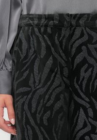 Crna suknja s teksturiranim uzorkom životinjskog printa u srebrnim točkicama. Dizajnirana s glatkim pojasom i laganim materijalom, nudi drapirani izgled.