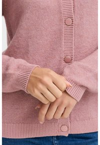 Cardigan rose clair en tricot doux, avec des poignets et un ourlet côtelés, fermeture à cinq boutons avec des boutons ronds pastel.