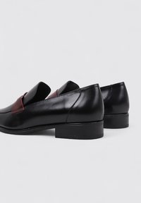 Mocasines de cuero negro con una correa de acento burdeos, con punta redondeada y un tacón bajo cuadrado. Textura suave y diseño elegante.