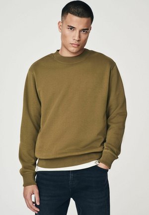 Olive green sweatshirt made of soft fabric, featuring a round neck and cuffs, paired with dark jeans. Simple design with a relaxed fit.