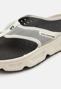 Lett Salomon flip-flop med en svart teksturert såle, hvit demping og en pustende mesh-overdel med en fremtredende logo.