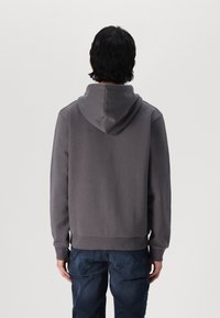 Felpa grigia in cotone con cappuccio regolabile e polsini a coste. La parte posteriore presenta una texture liscia e dettagli di design minimi.