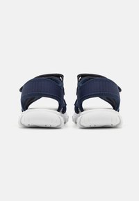 Námořnické modré sandály s texturovanými syntetickými popruhy, nastavitelnými úchyty na patě a kotníku, bílou gumovou podrážkou a minimalistickým designem.