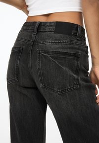 Zwarte denimbroek met hoge taille, twee achterzakken en een gestructureerde afwerking, die een getailleerd silhouet en minimale branding benadrukt.