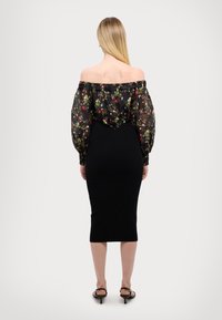 Φόρεμα off-the-shoulder με διαφανή μαύρη floral επένδυση και στενή μαύρη φούστα, αναδεικνύοντας μια σιλουέτα bodycon.