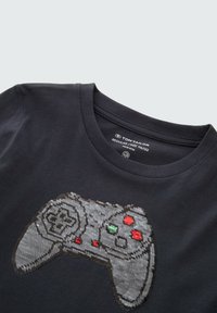 Donkergrijze katoenen T-shirt met een pixelachtige ontwerp van een gamecontroller in grijstinten, met rode en groene accenten rond de knoppen.