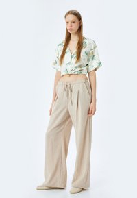 Afgeknipte, overhemd met groene palmbladprint; gecombineerd met losse, beige, hooggetailleerde broek en geweven instap-schoenen.