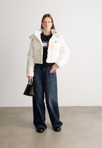 Biała krótka kurtka puchowa z stójką, czarny T-shirt z grafiką, luźne ciemnoniebieskie dżinsy i mała czarna torebka.