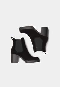 Stivaletti alla caviglia in suede nero con pannelli laterali elasticizzati, un robusto tacco a blocco e linguette per un facile indossamento. Superficie liscia con accenti minimi.