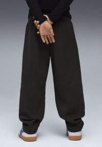 Sorte, løstsiddende sweatpants med elastisk talje, der har indsnævrede manchetter. Båret med en kombination af blå og hvide fodtøj.