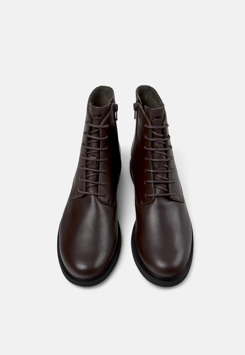 Botas cortas de cuero marrón con un acabado liso, con cordones en la parte delantera, detalle de cremallera y punteras redondas, sobre un fondo neutro.