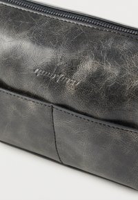 Μαύρο πορτοφόλι με υφή και εμφάνιση σκασμένου δέρματος, με φερμουάρ ως κλείσιμο. Διαθέτει μπροστινή θήκη και ανάγλυφο λογότυπο της μάρκας.