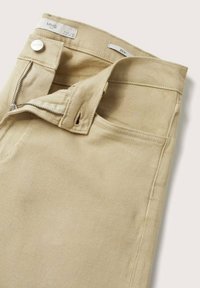 Pantalones de mezclilla beige con cremallera, cierre de botón metálico y etiquetas. Presentan una textura suave y un diseño clásico de cinco bolsillos.