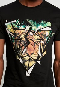 Camiseta negra de algodón con estampado de tigre geométrico y acentos de follaje verde, utilizando colores vibrantes y formas angulares en blanco.