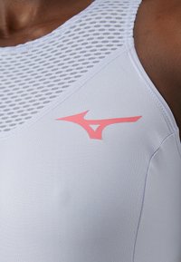 Top de desporto em lilás claro com um design de malha texturizada, apresentando um detalhe em rosa no peito e um acabamento de tecido liso.