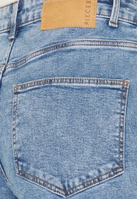 Světle modré džíny vyrobené z denimu, které mají jedno zadní kapsu s oranžovým švem a hnědou koženou etiketou připevněnou na pásku.