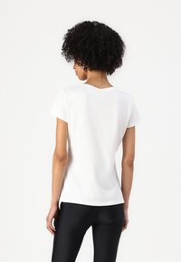 T-shirt bianco aderente con maniche corte, scollatura rotonda e texture di cotone morbido, abbinato a leggings neri.