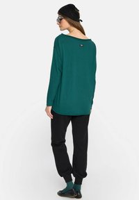 Zielona bluzka z długim rękawem i niskim dekoltem z tyłu, w połączeniu z czarnymi dresami. Charakteryzuje się luźnym krojem i subtelnym detalem na dekolcie.