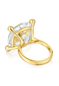 Złoty pierścień z dużym, przejrzystym kamieniem szlachetnym w kształcie trójkąta, mocowanym za pomocą czterech zaokrąglonych łapek, widoczny z bocznego, ukośnego kąta na białym tle.