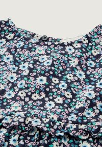 Blumenkleid mit navy Hintergrund, das kleine rosa, weiße und blaue Blumen zeigt. Mit rundem Halsauschnitt und einem schwarzen Knopf sowie einem rüschierten Saum.