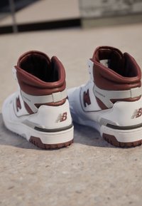 High-Top-Sneaker mit einem weißen synthetischen Obermaterial, braunen Lederelementen und einer strukturierten Gummisohle. Mit einem auffälligen 'N'-Logo.