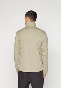 Beige jacket with a high collar, smooth texture, long sleeves, and side zippers, designed for versatility in casual wear.