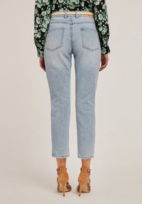 Jasnoniebieskie dżinsy w tapered fit, z dwiema tylnymi kieszeniami i podwiniętym dołem, noszone z camelowymi sandałami na obcasie.