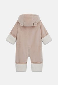 Monos de felpa suave en color beige con puños y capucha forrados de piel blanca. Cuenta con un cierre de cremallera en la parte posterior y detalles de orejas redondeadas en la capucha.