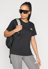 Μαύρο κοντομάνικο μπλουζάκι με στρογγυλή λαιμόκοψη και λογότυπο στο αριστερό στήθος, συνδυασμένο με γκρι κολάν και μαύρο σακίδιο πλάτης.