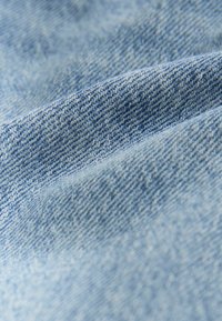 Lichtblauw denimstof met een gestructureerde weving. Het oppervlak vertoont subtiele kleur- en patroonvariaties die typisch zijn voor denim.